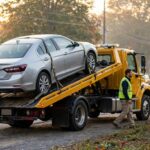 Flatbed tow truck with a car secured on the bed along a Northern Virginia road at sunrise